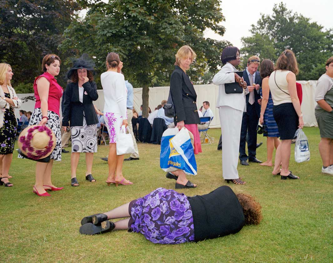 A woman lies on the grass next to a queue for the toilet at the