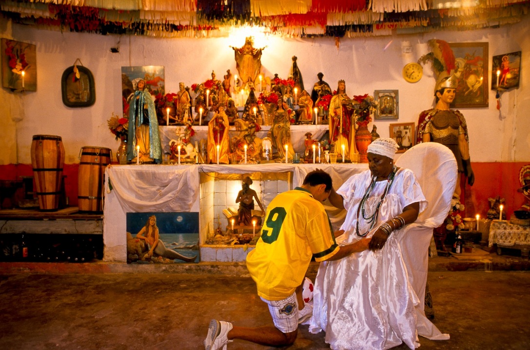   یک کشیش مذهب       یک کشیش مذهب حیوان پرستی Candomble افریقایی در حال تبرک و دعاخوانی برای یک برزیلی است که آمده است از دعای این کشیش برای پیروزی برزیل در جام جهانی کمک بگیرد.