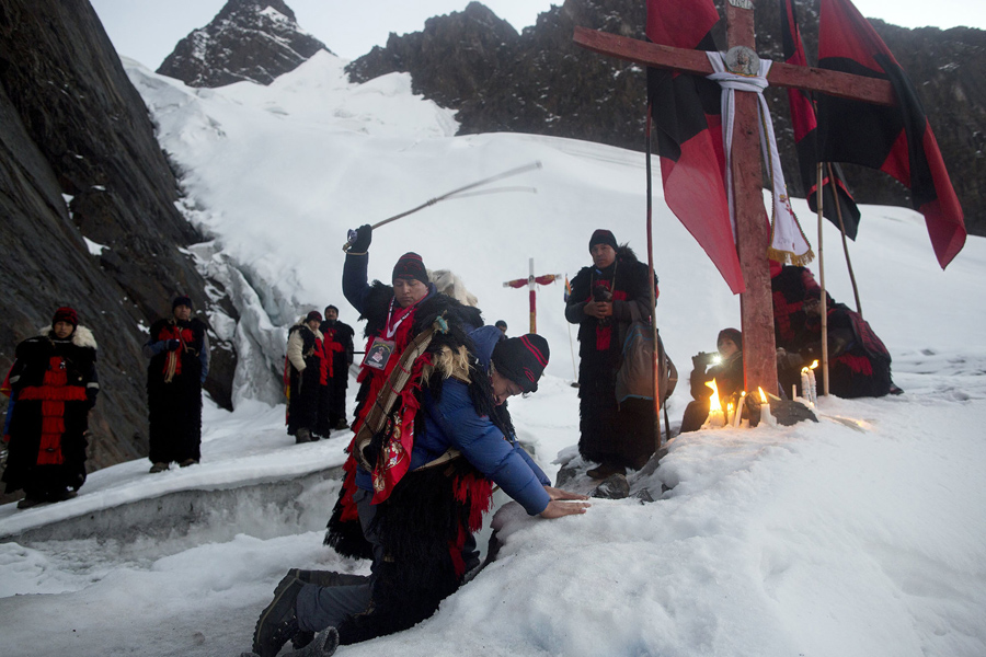 In this May 24, 2016 photo, an "ukuku" pledge places his hands on the ice of the Qullqip'unqu mountain glacier, kneeling before a cross as he is whipped three times by an ukukus leader, in an induction ceremony, as part of the syncretic festival Qoyllur RitÃ­i, translated from the Quechua language as Snow Star, in the Sinakara Valley, in Peru's Cusco region. New recruits promise to make the pilgrimage three years in a row. (AP Photo/Rodrigo Abd)